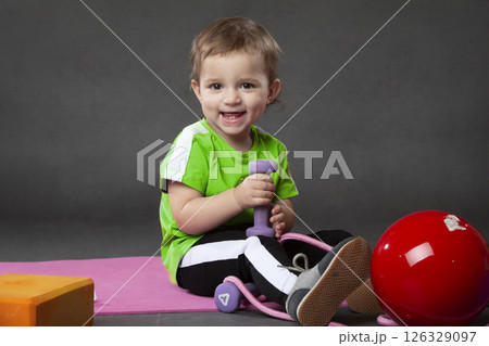Two year old girl doing sports posing with skipping rope and ball on grey background.Sports activities with little kids. 126329097