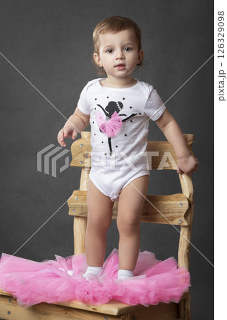 Little girl takes off her ballet tutu and looks at the camera on a gray background. 126329098