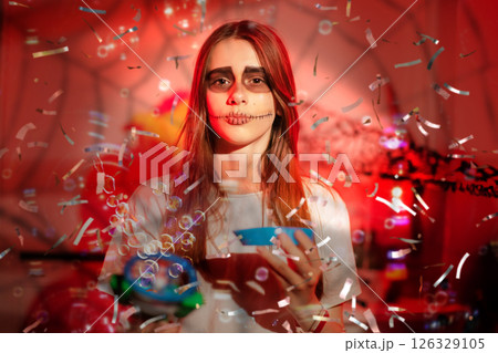 A teenage girl blows bubbles on Halloween with a skull painted on her face. 126329105