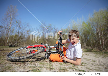 A boy is laying on the ground next to a broken bicycle. He is holding onto the handlebars and laughing 126329108