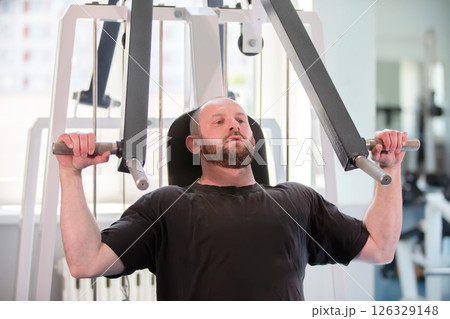 A man is working out at a gym, lifting weights and using a machine. He is focused and determined, likely trying to improve his strength and fitness 126329148
