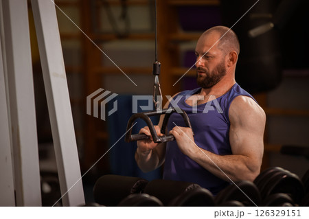 A man is working out with a weight machine. He is wearing a blue tank top and has a beard 126329151