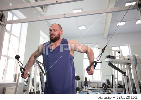 Male athlete bodybuilder exercising in the gym. Strength training on a cable machine. Male athlete bodybuilder exercising in the gym. Strength training on a cable machine. 126329152