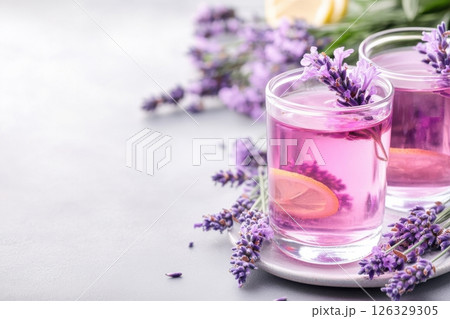 A refreshing and elegant beverage photography featuring lavender lemonade in clear glass tumblers garnished with fresh lavender sprigs and lemon slices.  126329305