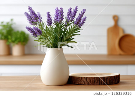A rustic kitchen scene featuring a white ceramic vase filled with fresh purple lavender stems on a wooden table. The minimalist composition includes a natural wood slice coaster. 126329316