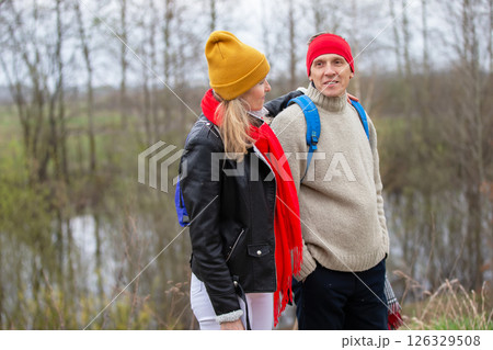 Active elderly Caucasian couple hiking with backpacks enjoying their adventure. They sit with their backs to the camera. 126329508