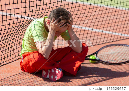 The boy lost the tennis competition. The child sits at the net with a racket. Psychology of sports in childhood. The boy lost the tennis competition. The child sits at the net with a racket. Psychology of sports in childhood. 126329657