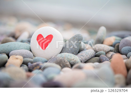 White stone with a painted red heart on a background of gray sea pebbles. White stone with a painted red heart on a background of gray sea pebbles. 126329704