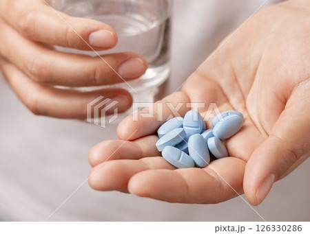 Woman in white t-shirt holding blue pills in cupped hand and water glass in hand closeup 126330286