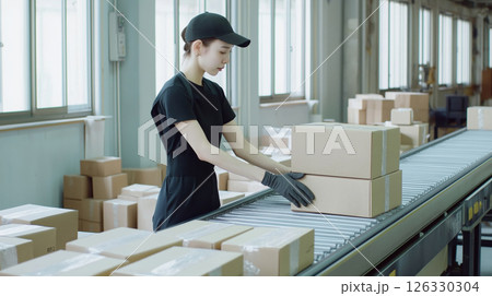 Female postal worker sorting packages on conveyor belt in distribution warehouse 126330304