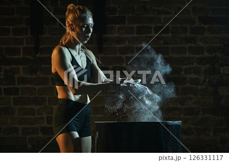 Focused female athlete prepares for lift by clapping chalked hands, sending powder cloud into air with tension and anticipation before workout. 126331117