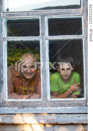Grandfather and grandson looking out of the window of a village house and smiling. Father's Day. Boy and man in the window. 126331228