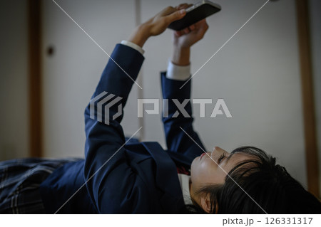 和室内で寝そべってスマホを見る女子高生　いじめ　不登校　SNSトラブル　社会問題 126331317