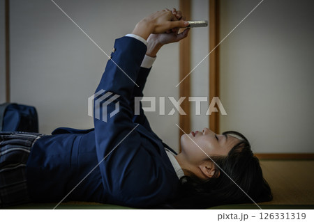 和室内で寝そべってスマホを見る女子高生　いじめ　不登校　SNSトラブル　社会問題 126331319
