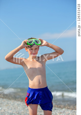 A teenage boy in swimming goggles put his hands behind his head and admires the sea. A teenage boy in swimming goggles put his hands behind his head and admires the sea. 126331418