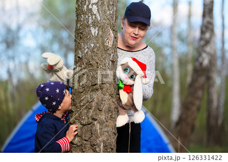 Grandmother plays with her grandson outdoors. Shows soft toys and tells a fairy tale. 126331422