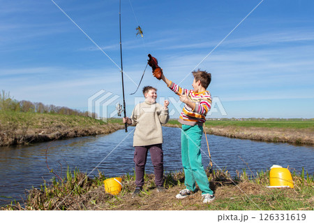 Funny fishing. Two of the boy's friends hooked an old shoe with a fishing rod and are laughing. Funny fishing. Two of the boy's friends hooked an old shoe with a fishing rod and are laughing. 126331619