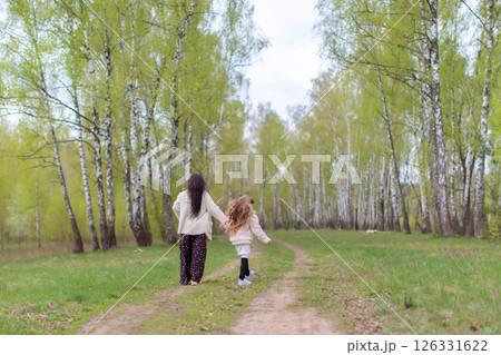 Mom and daughter are walking through a birch grove with their backs to the camera. Mom and daughter are walking through a birch grove with their backs to the camera. 126331622