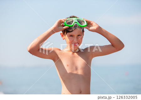 A teenage boy in swimming goggles put his hands behind his head and admires the sea. 126332005