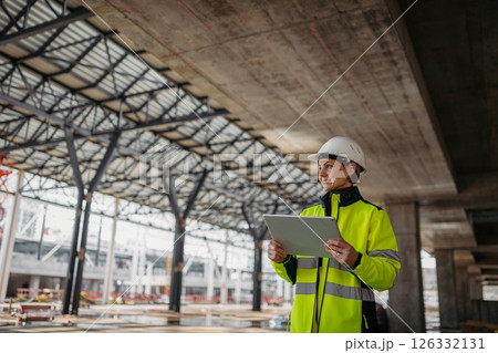 Female engineer checking building documentation on clipboard at construction site. 126332131