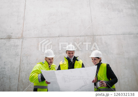 Team of engineers and construction workers reviewing blueprints, building site. 126332138