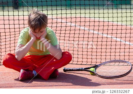 The boy lost the tennis competition. The child sits at the net with a racket. Psychology of sports in childhood. The boy lost the tennis competition. The child sits at the net with a racket. Psychology of sports in childhood. 126332267