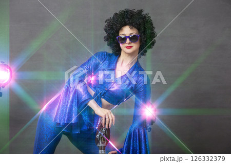 Girl comic pop star posing in black wig with toy guitar on blue background. Rock style of seventies Girl comic pop star posing in black wig with toy guitar on blue background. Rock style of seventies 126332379