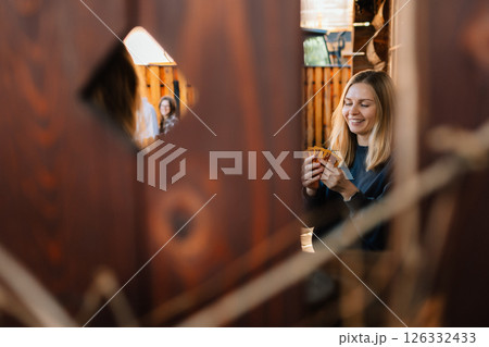 Young woman holding playing cards, smiling and peeking through wooden fence, enjoying card game with her friends in cozy outdoor setting. Female grasping playing cards, outdoor card game with friends Young woman holding playing cards, smiling and peeking through wooden fence, enjoying card game with her friends in cozy outdoor setting. Female grasping playing cards, outdoor card game with friends 126332433