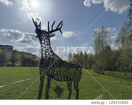 Metal Deer Sculpture Silhouetted Against the Bright Sun and Cloudy Sky 126332681