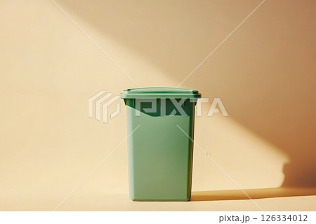 Green wheelie bin standing on beige background in sunlight Green wheelie bin standing on beige background in sunlight 126334012