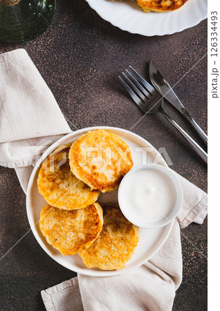 Appetizing potato fritters and sour cream on a plate on the table top and vertical view Appetizing potato fritters and sour cream on a plate on the table top and vertical view 126334493