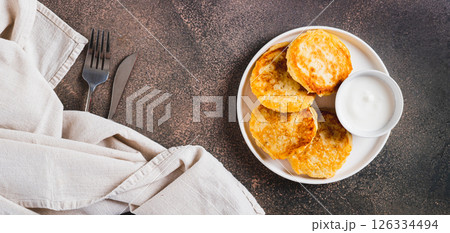 Appetizing potato fritters and sour cream on a plate on the table top view web banner Appetizing potato fritters and sour cream on a plate on the table top view web banner 126334494