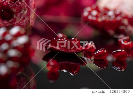 peeled ripe red pomegranate with juicy grains, The pomegranate fruit is reflected on the table, close up, side view 126334809