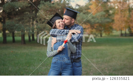 A joyful couple is celebrating their graduation in a beautiful outdoor setting surrounded by nature 126335821