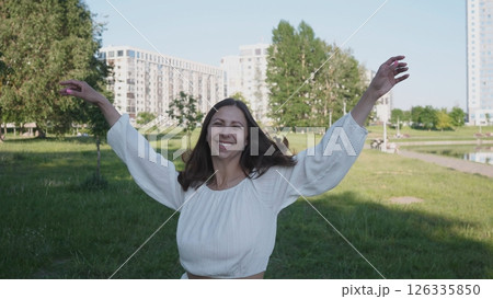 A joyful and carefree woman happily enjoying a sunny day in a vibrant green park with tall buildings in the background A joyful and carefree woman happily enjoying a sunny day in a vibrant green park with tall buildings in the background 126335850