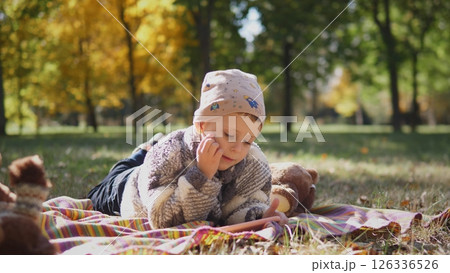 A thoughtful and curious child is happily enjoying reading on a cozy blanket in a vibrant autumn park setting 126336526