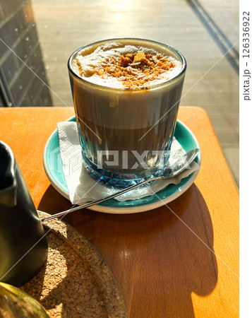 Cup of cappuccino with delicate foam art bathed in golden sunlight, placed on wooden table. Cozy atmosphere ideal for travel cafe lifestyle and social media content. Vertical. Cup of cappuccino with delicate foam art bathed in golden sunlight, placed on wooden table. Cozy atmosphere ideal for travel cafe lifestyle and social media content. Vertical. 126336922