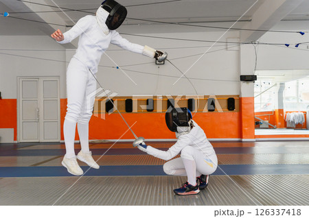 Female fencers making simultaneous epee hit in indoor duel. Female fencers making simultaneous epee hit in indoor duel. 126337418