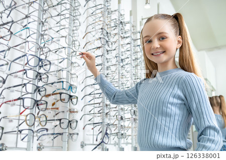 Long-haired caucasian girl choosing new eyeglasses in an optic shop 126338001