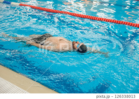 Man in black swimming cap swimming backstroke in the pool Man in black swimming cap swimming backstroke in the pool 126338013