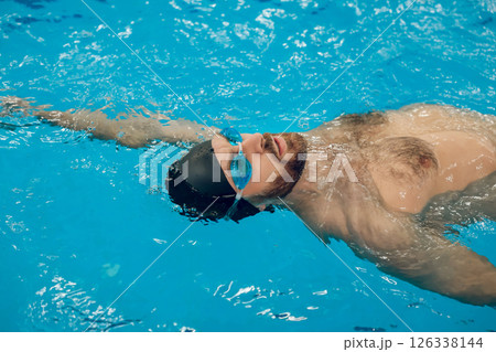 Man in black swimming cap swimming backstroke in the pool Man in black swimming cap swimming backstroke in the pool 126338144