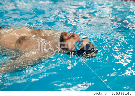 Man in black swimming cap swimming backstroke in the pool Man in black swimming cap swimming backstroke in the pool 126338146