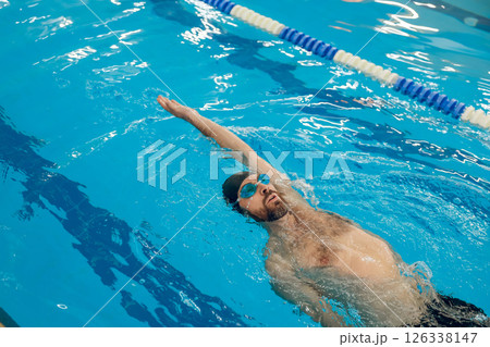 Man in black swimming cap swimming backstroke in the pool Man in black swimming cap swimming backstroke in the pool 126338147