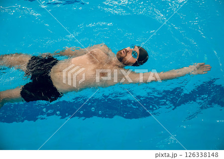 Man in black swimming cap swimming backstroke in the pool 126338148