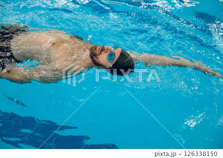 Man in black swimming cap swimming backstroke in the pool Man in black swimming cap swimming backstroke in the pool 126338150