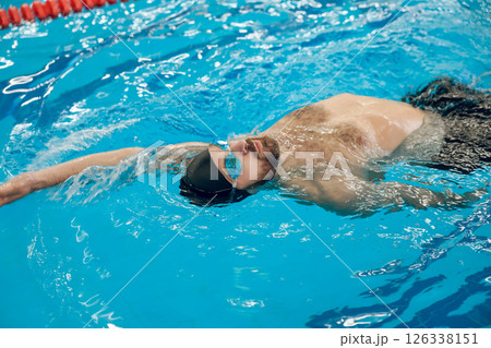 Man in black swimming cap swimming backstroke in the pool 126338151
