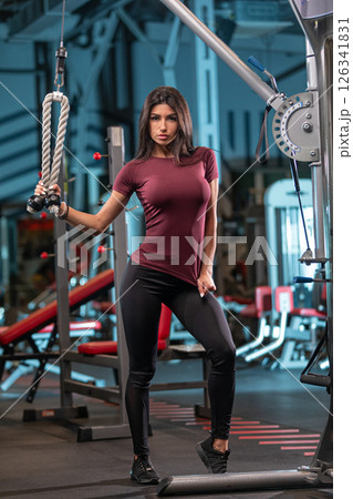 fitness enthusiast showcases strength while using gym equipment. Dressed in stylish activewear she emphasizes a focus on health and fitness in a modern gym environment. 126341831