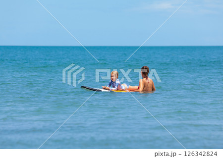 Happy baby girl - young surfer ride on surfboard with fun on sea waves. Active family lifestyle, kids outdoor water sport lessons and swimming activity in surf camp. Summer vacation with child. 126342824