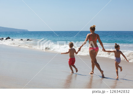 Happy family - mother, kids hold hands and run with fun along edge of sunset sea on sand beach. Active parents and people outdoor activity on tropical summer vacations with children 126342832