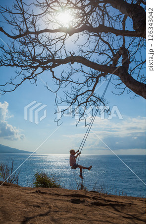 Happy girl have fun swinging high in mid air. Flying up upside down on rope swing on sea beach. Travel adventure on paradise tropical island. Family lifestyle, activity on summer vacation with kids. Happy girl have fun swinging high in mid air. Flying up upside down on rope swing on sea beach. Travel adventure on paradise tropical island. Family lifestyle, activity on summer vacation with kids. 126343042